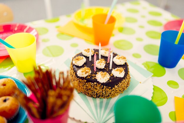 Pastel de cumpleaños en la mesa con vasos de colores