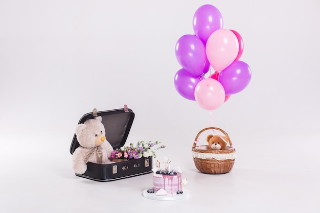 Pastel de cumpleaños, oso de peluche en suitecase vintage y globos aislados sobre fondo blanco