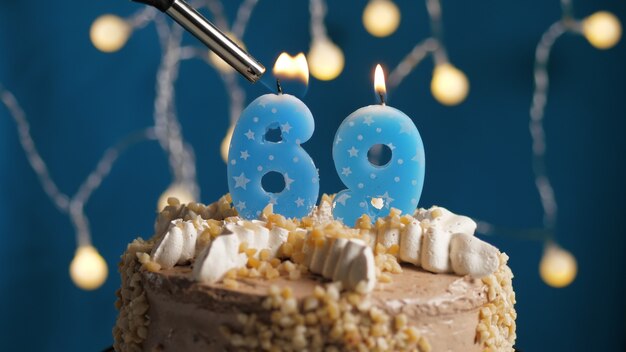 Pastel de cumpleaños con vela número 69 en backgraund azul prendido fuego por encendedor. de cerca