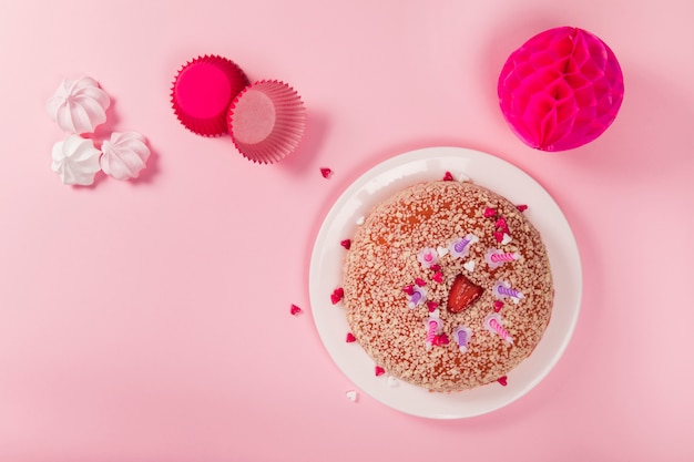 Pastel de cumpleaños con velas; zephyrs; soporte para cupcakes de papel y bolas de papel de nido de abeja pom-pom sobre fondo rosa