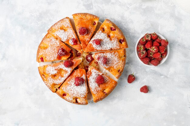 Pastel de frambuesa con azúcar en polvo y frambuesas frescas en una luz. Postre de bayas de verano.