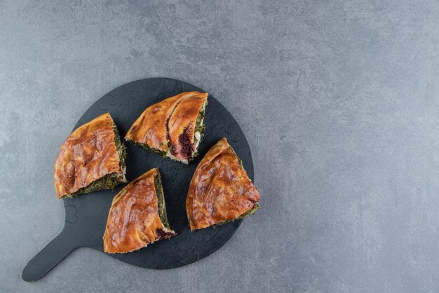 Pastel fresco en rodajas con verduras sobre tabla de cortar negra.