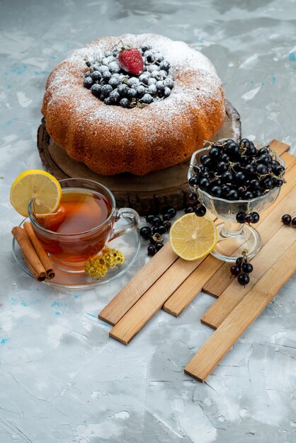 Un pastel de frutas de vista frontal delicioso y redondo formado con azul fresco, bayas y junto con una taza de té brillante, bizcocho de azúcar dulce