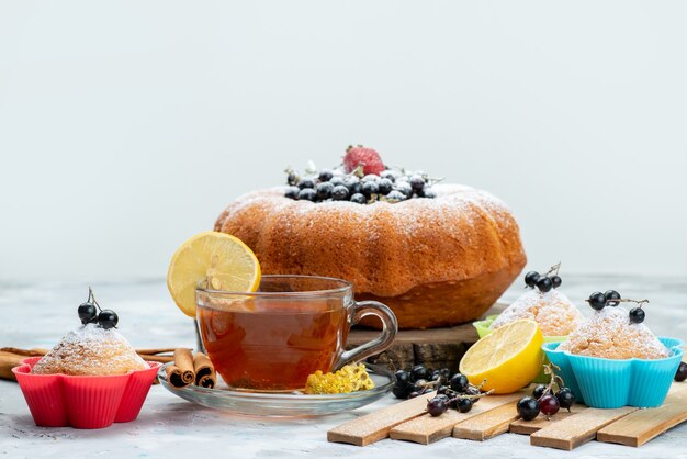 Un pastel de frutas de vista frontal delicioso y redondo formado con azul fresco, bayas y junto con una taza de té brillante, bizcocho de azúcar dulce