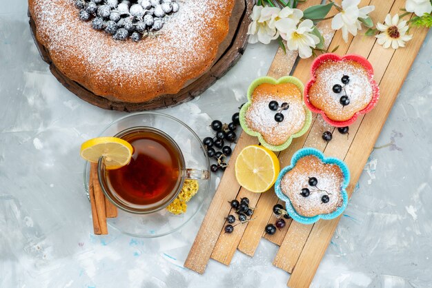 Un pastel de frutas de vista superior delicioso y redondo formado con azul fresco, bayas y junto con una taza de té en un pastel brillante