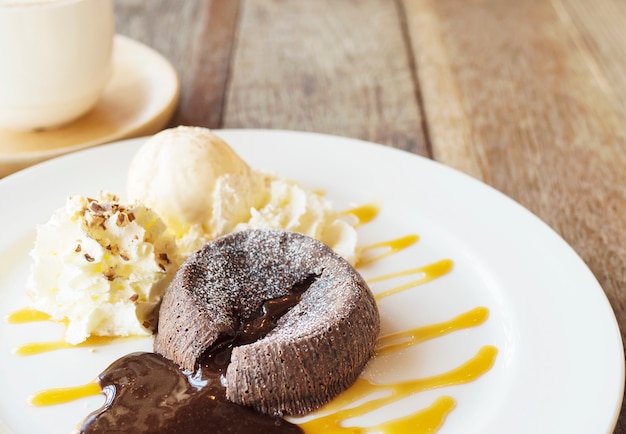 Pastel de lava de chocolate en un plato blanco con una taza de café en la mesa de madera vieja