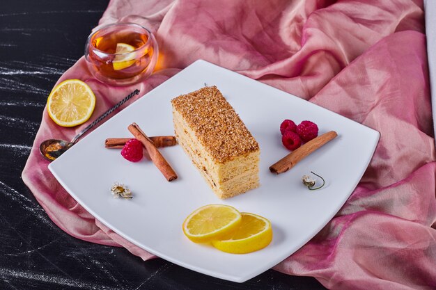 Pastel de miel con canela y frutas en plato blanco junto a mantel rosa.