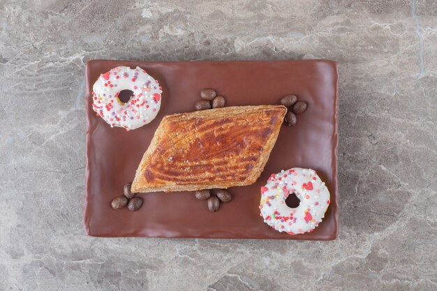 Pastel pequeño, granos de café y rosquillas del tamaño de un bocado en un plato sobre una superficie de mármol