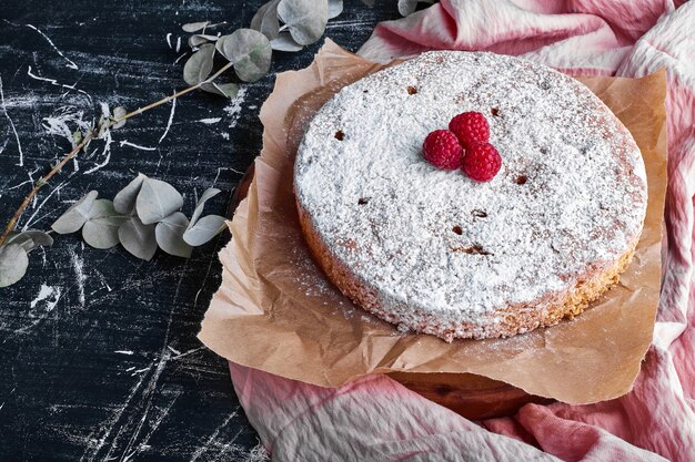 Pastel redondo con azúcar en polvo y frambuesas.