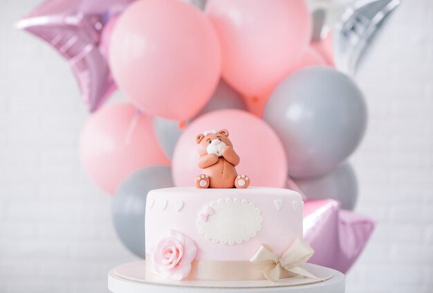 pastel rosa festivo con un arco y un oso en la parte superior de un fondo de globos