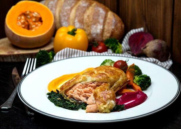 Pastel de salmón servido con hierbas asadas, verduras y salsa agria