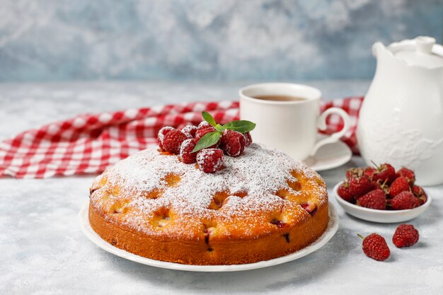 Pastel simple con azúcar en polvo y frambuesas frescas en una luz. Postre de bayas de verano.