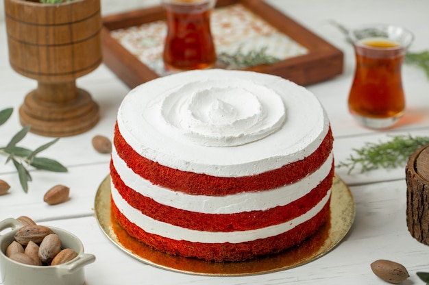 Pastel de terciopelo rojo con crema batida blanca y un vaso de té.