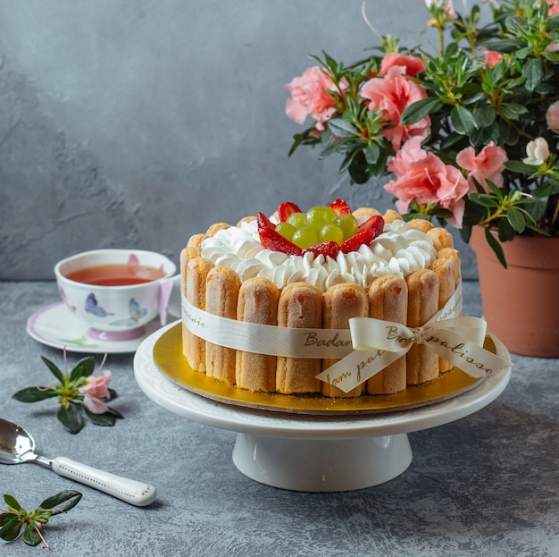 Pastel de tiramisú con lady finger cookies y bayas con una taza de té y flores.