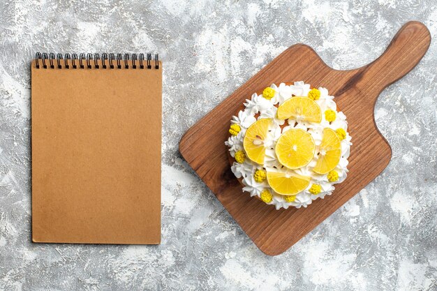 Pastel de vista superior con crema blanca y rodajas de limón en tabla de cortar y cuaderno vacío