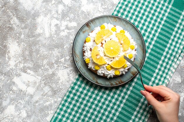 Foto gratuita pastel de vista superior con crema pastelera blanca y rodajas de limón en un plato redondo sobre un tenedor de mantel a cuadros verde y blanco en la mano femenina