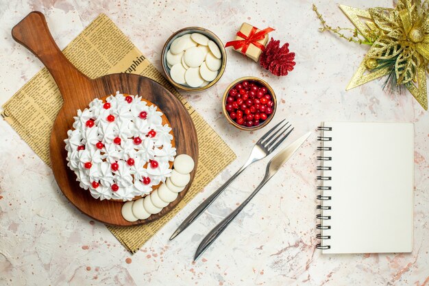 Pastel de vista superior con crema pastelera blanca sobre tablero de madera en periódico y adornos navideños