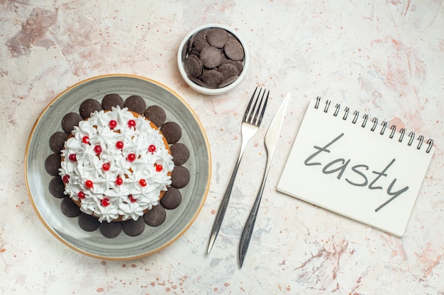 Pastel de vista superior con crema pastelera en placa ovalada chocolate en un tenedor y cuchillo de cena. sabrosa palabra escrita en el cuaderno