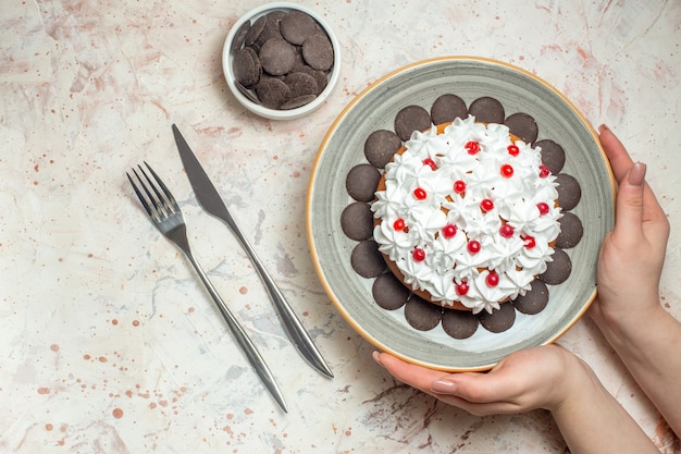 Pastel de vista superior con crema pastelera en placa ovalada en mano femenina chocolate en un tazón tenedor y cuchillo de cena