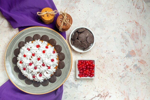 Pastel de vista superior con crema pastelera en plato ovalado galletas de mantón púrpura atadas con cuencos de cuerda con chocolate y bayas