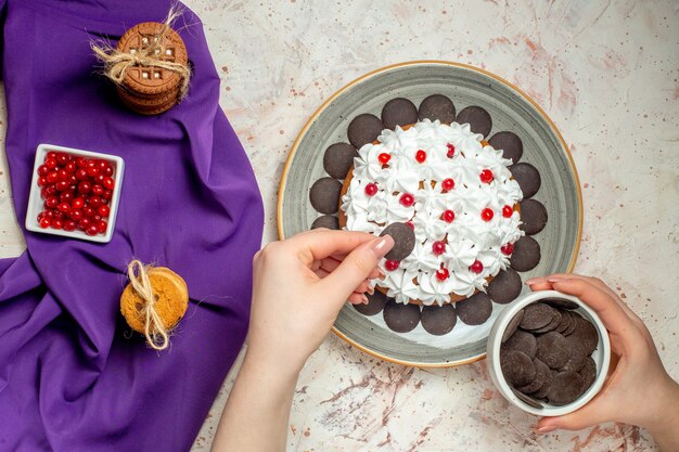 Pastel de vista superior en galletas de placa atadas con cuenco de cuerda con bayas en cuenco de chocolate de mantón púrpura en mano de mujer