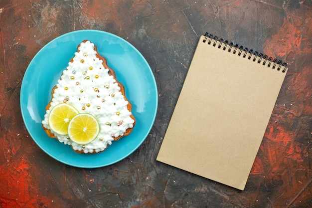 Pastel de vista superior con limón en el cuaderno de placa azul sobre fondo rojo oscuro