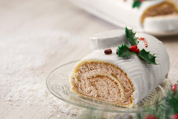 Pastel de yule log de chocolate blanco con luces navideñas y adornos en mesa de madera