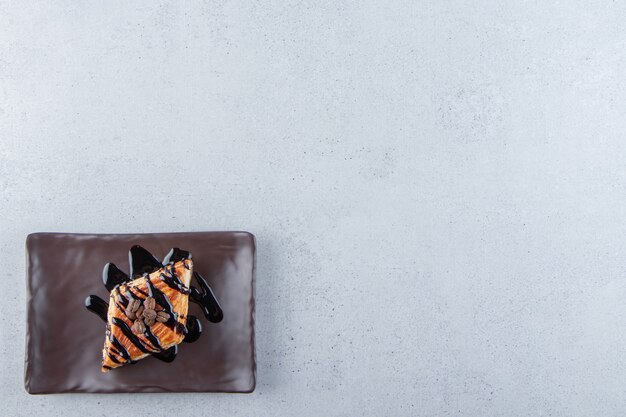 Pastelería dulce decorada con chocolate colocada en un plato oscuro. Foto de alta calidad