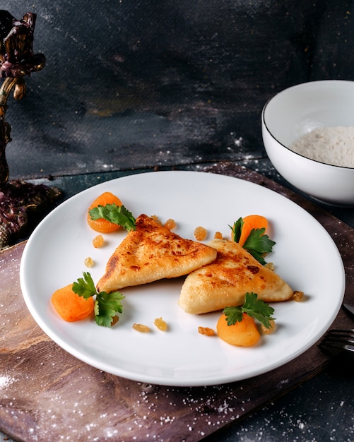 Foto gratuita pastelería sabrosa deliciosa junto con rodajas de zanahoria naranja hervida y hojas verdes dentro de un plato blanco sobre la superficie brillante