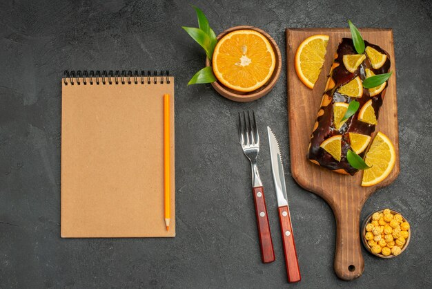 Pasteles blandos a bordo y limones cortados con hojas y cuaderno sobre mesa oscura