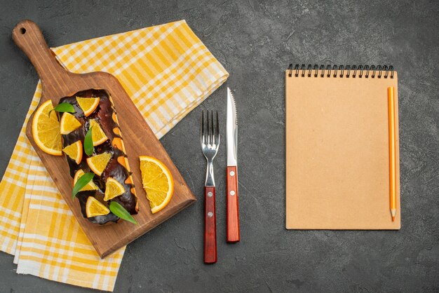 Pasteles blandos a bordo y limones cortados con hojas en una toalla verde junto al cuaderno