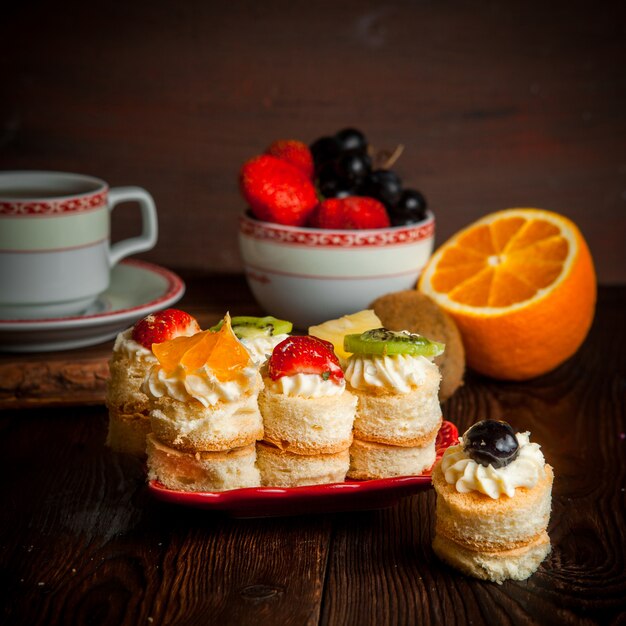 pasteles de crema y frutas con una taza de té y una bandeja de frutas y naranja en un plato