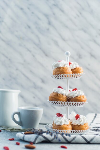 Pasteles frescos en el soporte de la torta con la taza y el alimento de la tuerca sobre superficie concreta