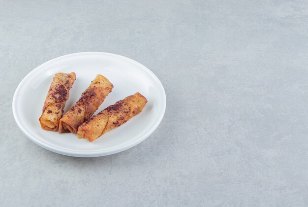 Pasteles fritos en forma de cigarro en un plato blanco.