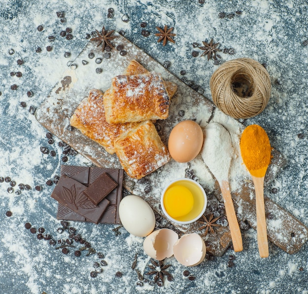 Pasteles con harina, chocolate, especias, huevos, vista superior de hilo en hormigón y tabla de cortar