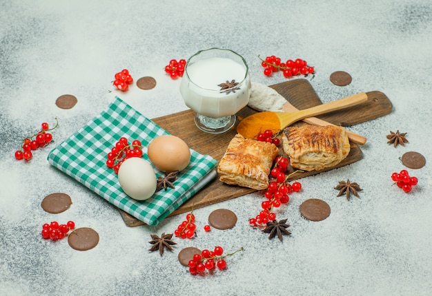 Pasteles con harina, grosellas, leche, huevos, especias, galletas Vista de ángulo alto en hormigón y tabla de cortar