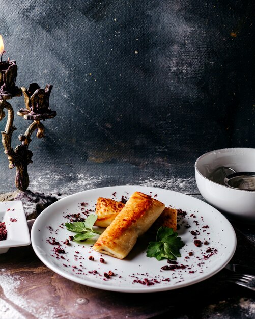 Pasteles poco con carne junto con hojas verdes y especias marrones dentro de un plato blanco sobre la superficie gris