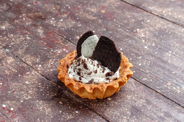 Pastelito con crema y galletas de chocolate aislado en marrón de madera, pastel biscuitt hornear color