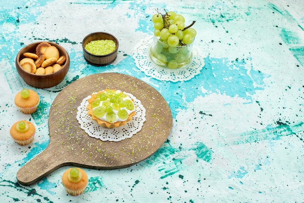 Pastelito con deliciosa crema y galletas de uvas verdes frescas y en rodajas aisladas en el escritorio de luz azul, pastel de fruta dulce azúcar