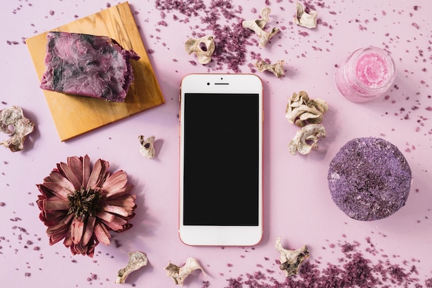 Pastilla de jabón; exfoliación corporal a base de hierbas; Flor seca y smartphone sobre fondo rosa