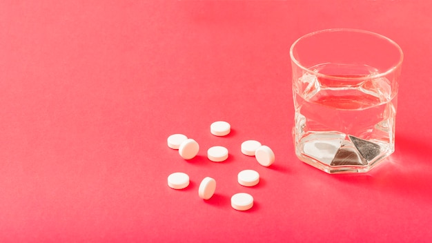 Foto gratuita pastillas blancas y vaso de agua sobre el fondo rojo