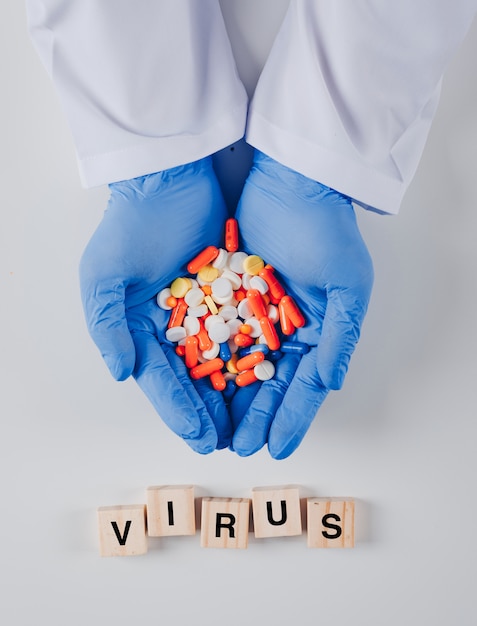 Foto gratuita pastillas dentro de las manos del médico con vista superior de texto de virus en un virus de superficie blanca