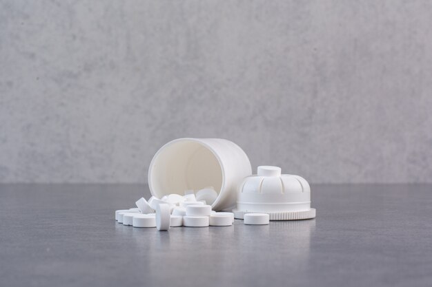 Pastillas médicas blancas de recipiente de plástico.