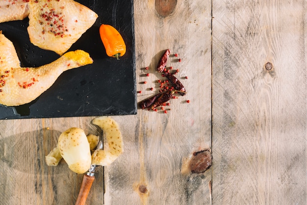 Patata pelada cerca de las piernas de pollo crudo