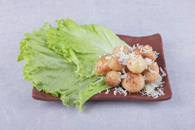 Patatas fritas decoradas con queso en placa marrón.