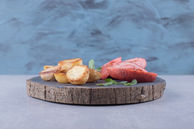 Patatas fritas y embutidos sobre pieza de madera.