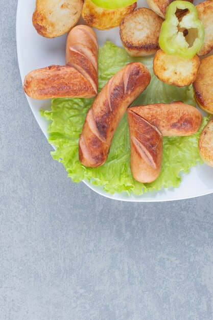 Patatas fritas frescas y salchichas en un plato blanco.