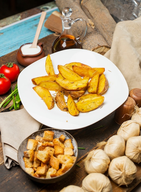 Patatas fritas con hierbas y yogurt en plato blanco con galletas de pan alrededor.