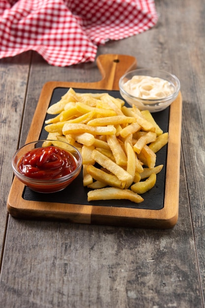 Patatas fritas con ketchup y mayonesa sobre mesa de madera