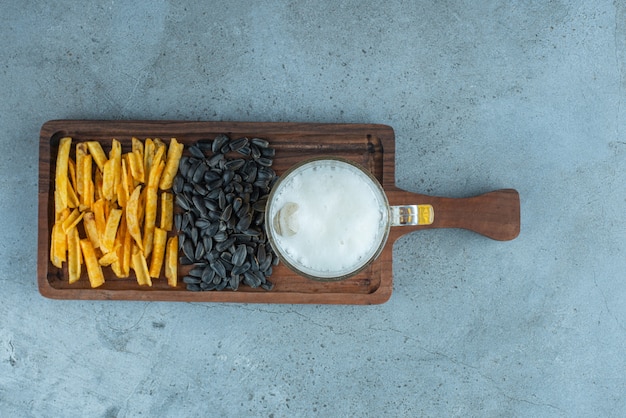 Patatas fritas, pipas de girasol y un vaso de cerveza en un tablero, sobre la mesa azul.